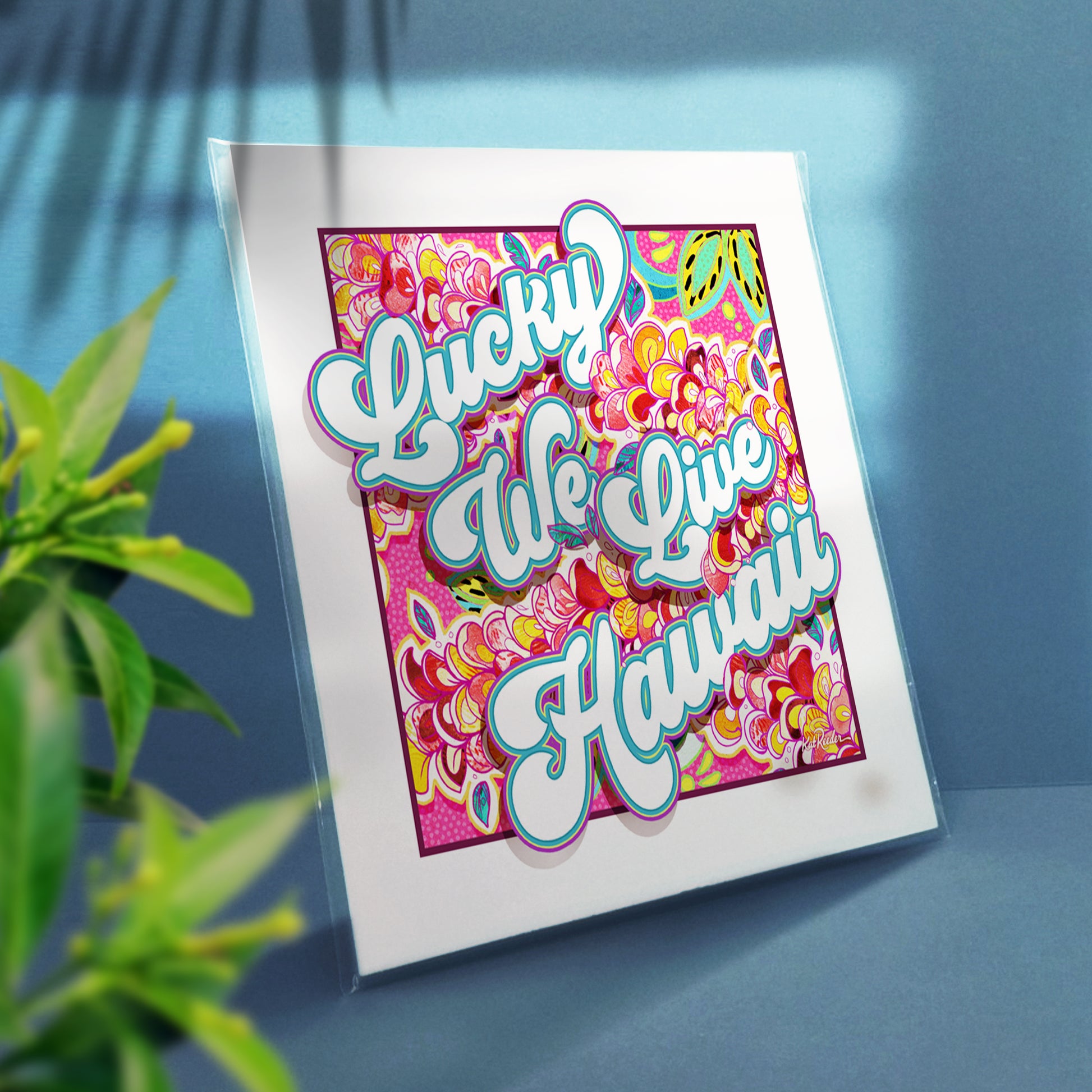 3/4 view of a square print of an sign that reads  "lucky we live hawaii", featuring bubbly fonts and floral lei patterns