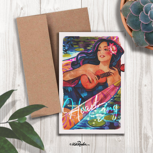 5x7 greeting card featuring an illustration of a blue haired hula girl playing ukulele in a hammock at night next to a pond. Text on card reads "You make my heart sing"